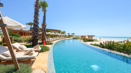 Long, curved resort pool bordering a white sand beach and turquoise ocean under a bright, clear blue sky