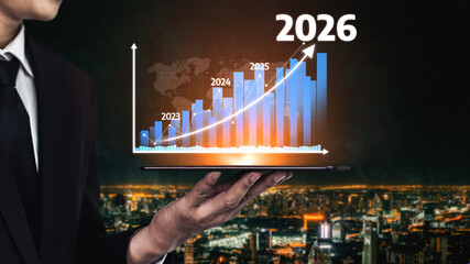 A businessman holds a laptop displaying a growth graph spanning from 2023 to 2026, symbolizing...