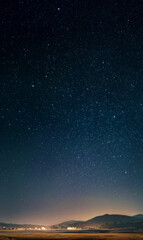 Fototapeta premium A breathtaking view of a starry night sky over a calm, lit rural setting.