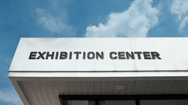 Exhibition Center word sign clearly displayed on the large commercial venue facade beneath a clear blue sky, signifying a facility dedicated to hosting trade shows, expos, and public displays.