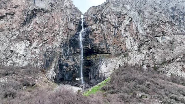 A spectacular narrow waterfall dropping from a narrow cleft between two towering, steep mountain rock faces and cliffs
