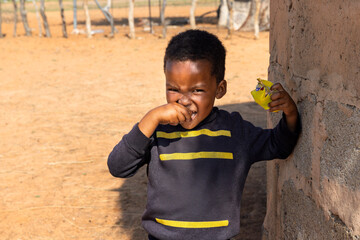 hungry african child in the village, eating biscuits next to the house in the yard