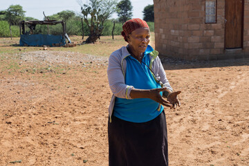 village old african woman with hands forward gesture, standing in the yard at home