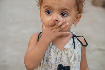 Surprised little girl covering her mouth with hand while standing outdoors and looking amazed with wide eyes