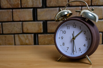 Naklejka premium Vintage alarm clock placed on a wooden desk with warm brick wall background. Classic still life composition with negative space on the right side, perfect for time, routine, productivity concept