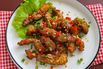 Closeup of a plate of garlic fried pork belly, a savory and crispy dish garnished with chopped red chilies and fresh scallions.