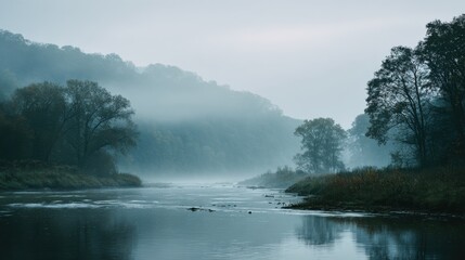 Fototapeta premium A calm river flows through a foggy valley, surrounded by trees. The morning light creates a peaceful atmosphere. Mist rises gently from the water, enhancing the tranquil scene.