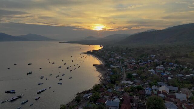 Aerial view of coastal fishing village in Indonesia at sunset, with many boats in the bay.
