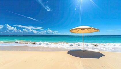 Bright sunny day at the tropical beach with a closed beige umbrella standing on wet yellow sand and turquoise ocean waves gently rolling in under a clear blue sky with wispy clouds and sun glare