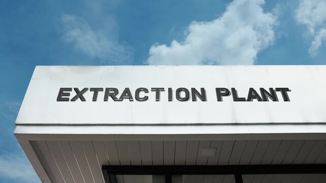 Extraction Plant word sign prominently displayed on the large industrial building facade beneath a clear blue sky, signifying a factory dedicated to separating and refining raw materials or substances