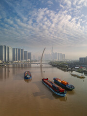 Transporting containers on barges Saigon River early sunny clear morning with Ho Chi Minh City suspension bridge, modern architecture and landmark in the background
