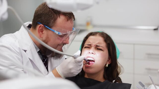 Qualified male dentist carefully drills into a woman tooth to remove caries and make a filling. Woman undergoing treatment in a dental clinic. High quality FullHD footage