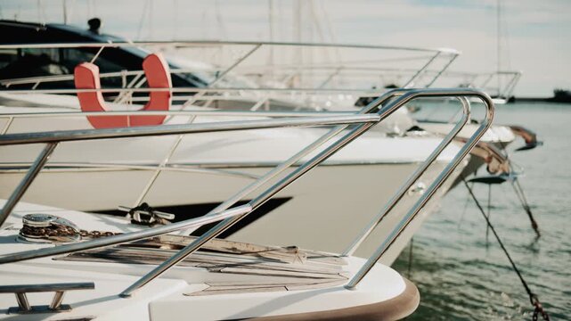 Close up of chrome railing and wooden deck of a luxury yacht docked in a marina under golden light