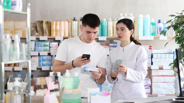 Young male customer buying and scanning qr code for gel in small pharmacy, chatting with female pharmacist