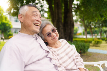 Fototapeta premium Elderly Asian couple enjoying time together on park bench, showing love and care.