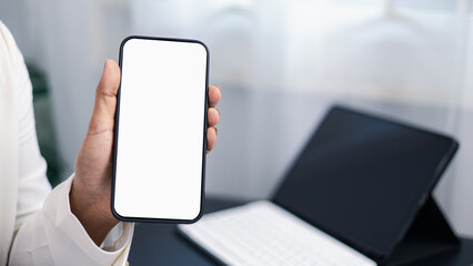 Businessman holding smartphone with blank screen mockup in modern office workspace