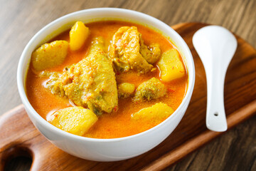 A view of chicken and potato curry served in a white bowl on a wooden table.