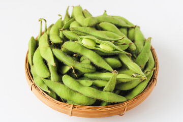 A basket filled with vibrant green edamame pods, with one pod split open, displayed on a clean white background. A popular and healthy snack.