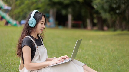 A student with headphones typing on a laptop in a university park.