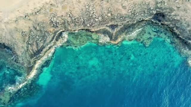 Drone shot over Lanzarote cliff egde with ocean sea waves breaking against rocks in Puerto Del Carmen - crystal clear blue water - right to left