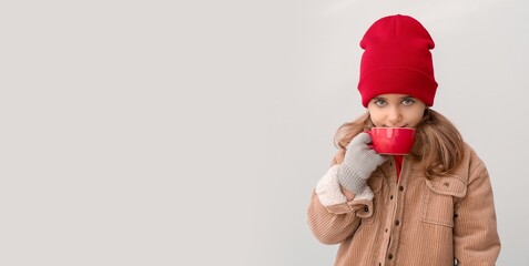 Cute little girl in winter clothes drinking hot chocolate on light background with space for text