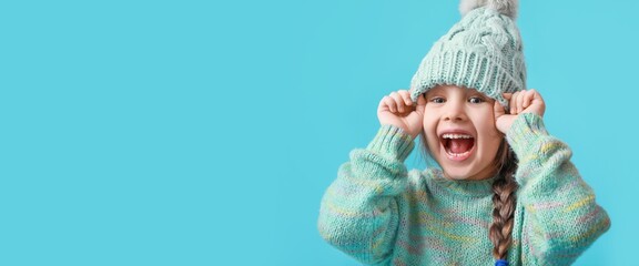Happy little girl in winter clothes on blue background with space for text