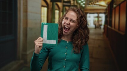 Woman smiling holding learner's driver sign on city street expressing pride and achievement outdoors.
