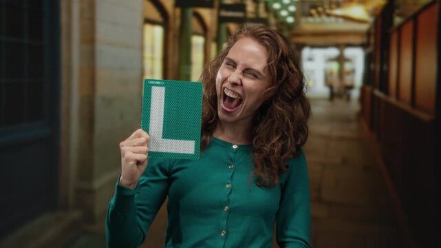 Woman smiling holding learner's driver sign on city street expressing pride and achievement outdoors.