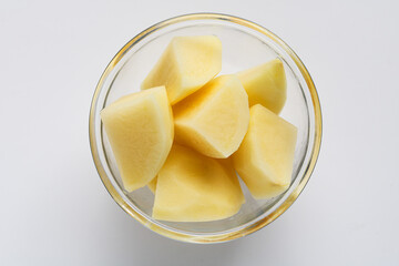 Raw yellow potatoes cut into large chunks and displayed in a clear glass bowl, isolated on a light background.