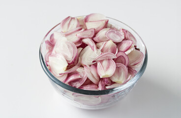 A pile of raw sliced shallots in a clear glass bowl, isolated on a white background.