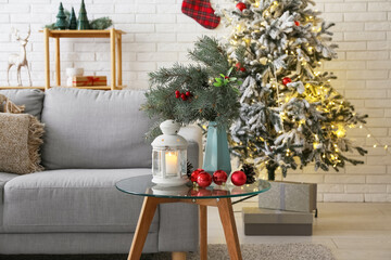 Glass coffee table with glowing lantern, Christmas baubles and fir branches in festive living room, closeup