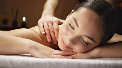 Obraz premium A woman receives a relaxing massage, her eyes closed in serene contentment. A skilled therapist's hands gently press her shoulders, promoting relaxation and stress relief.