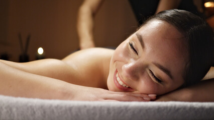 Obraz premium A woman lies on a massage table, smiling serenely. Her relaxed posture and closed eyes suggest a deep sense of calm and relief.