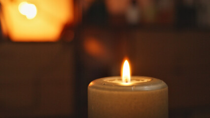 A single lit candle in a dimly lit room, casting a warm glow. The flame flickers gently, creating a serene and intimate atmosphere.