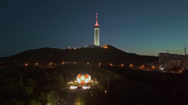 Dolly-in shot from Laotong Park approaching Dalian TV station tower as sunset lights illuminate the area