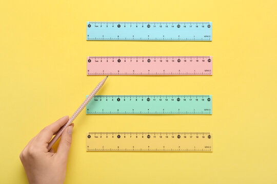 Female hand with pencil and rulers on yellow background