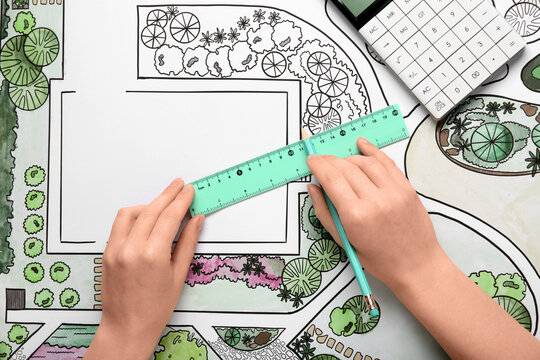 Female hands with pencil, ruler and calculator on landscape design drawing background - Powered by Adobe