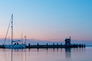 Sailboat resting at a tranquil dock during sunset on a calm body of water with pastel sky hues