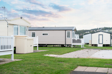 Fototapeta premium Cozy mobile homes situated at a tranquil campsite surrounded by greenery during a serene sunset hour