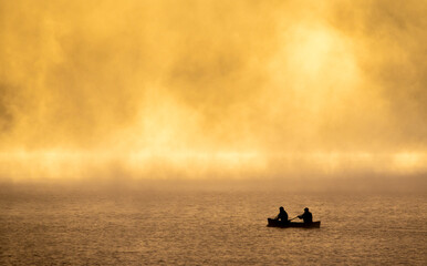 A small boat rowing silently through the golden morning mist