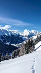 Snow-covered mountain valley viewed from a snowy slope, with footprints in the foreground and a clear blue sky