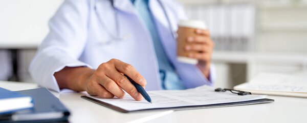 Professional doctor holding a hot coffee drink cup.doing paperwork checking medical documents at...