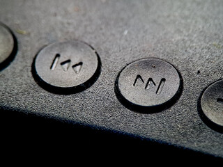 Textured black surface showcasing round buttons with symbol for rewind or fast forward action.