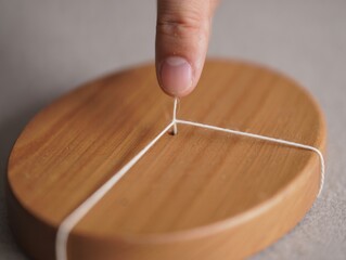 Finger pulling a string taut across a wooden circular object