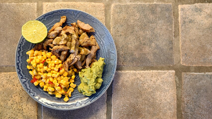 pork fajitas, corn and guacamole on a blue plate with a rustic tiled background  