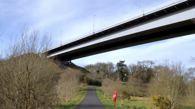 A large bridge span passes over a path through parkland