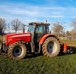 A red tractor towing a yellow dump truck across a field, showcasing farm machinery in action.