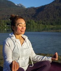 Person doing yoga in front of a lake with eyes closed