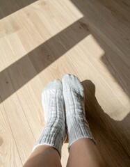 Person wearing wool socks resting on wooden floor with sunlight shadows.