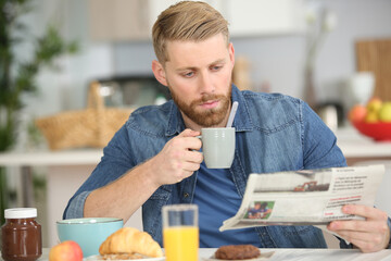 handsome young man having breakfast and reading newspaper at home